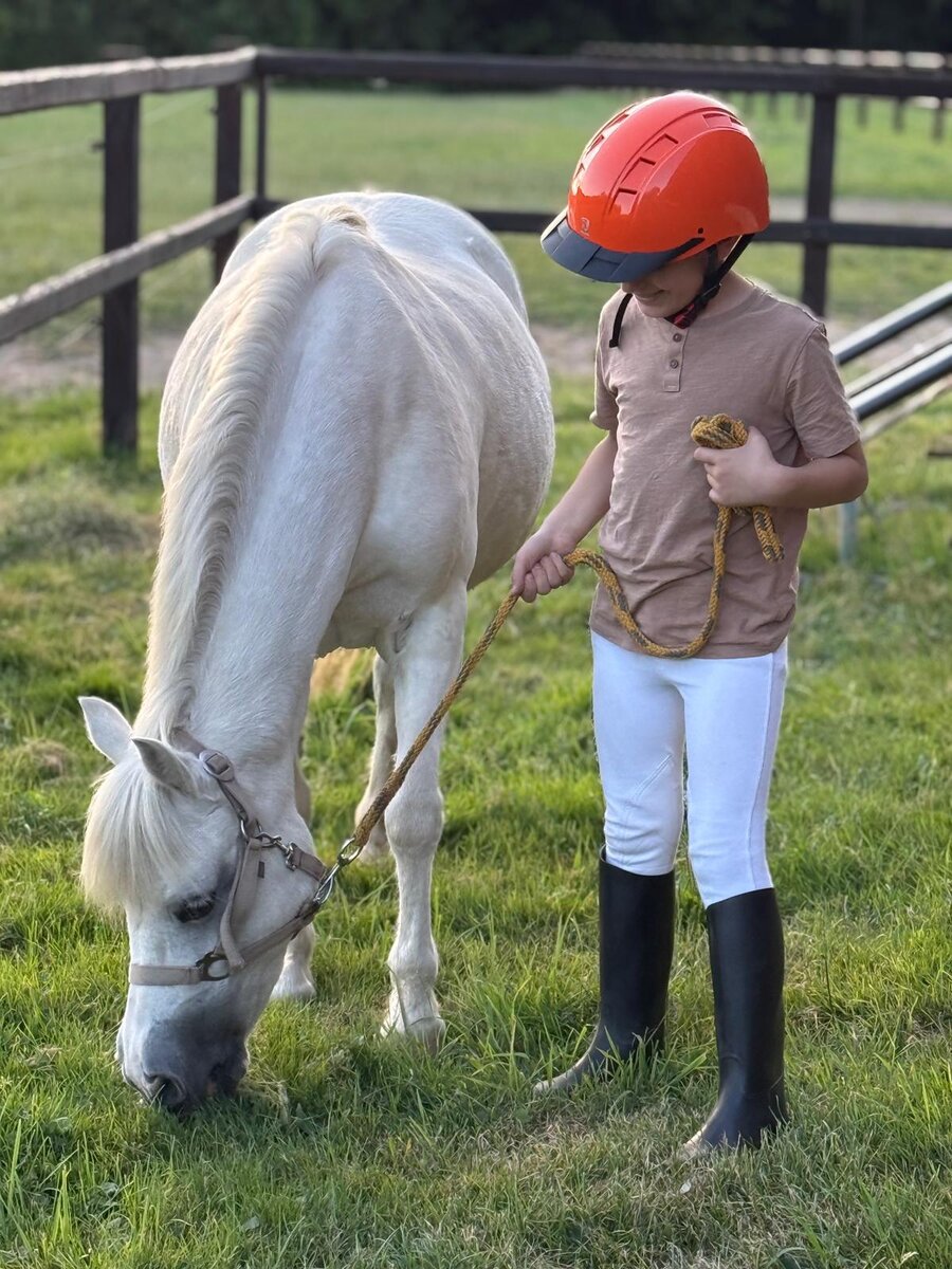 Een jonge ruiter met een witte pony in de wei bij Manege M. Meijer